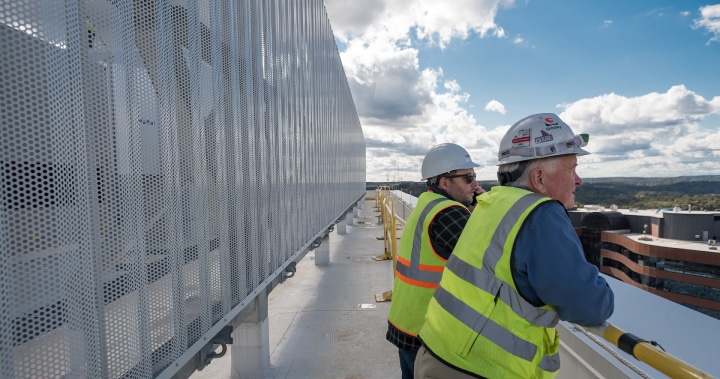 Two workers on rooftop wearing hardhats and safety vests